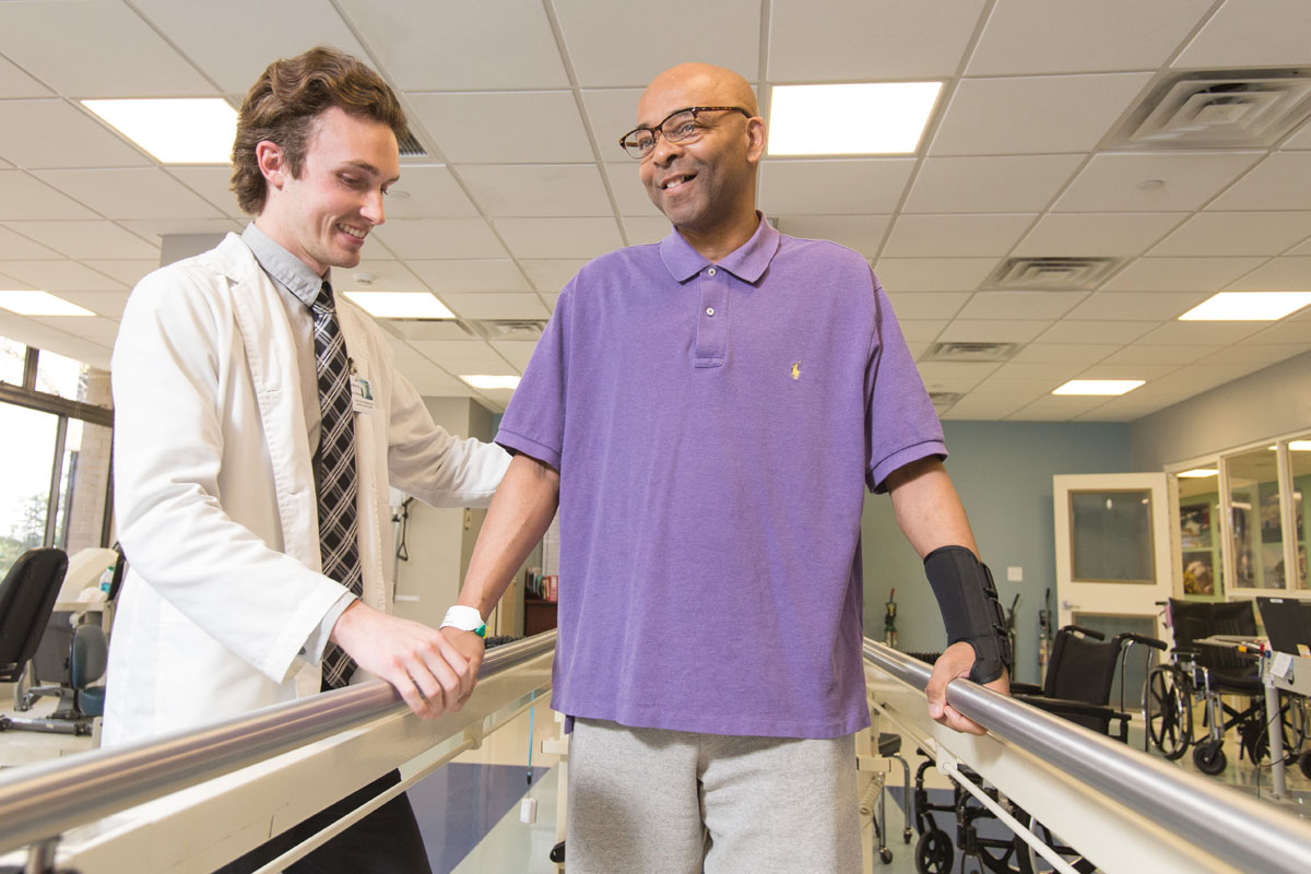 Therapist helps patient on parallel bars